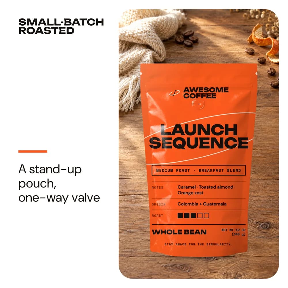 The Launch Sequence bag on a wooden table with a knit throw, coffee beans and orange peel, headline Small-batch roasted and the line A stand-up pouch, one-way valve